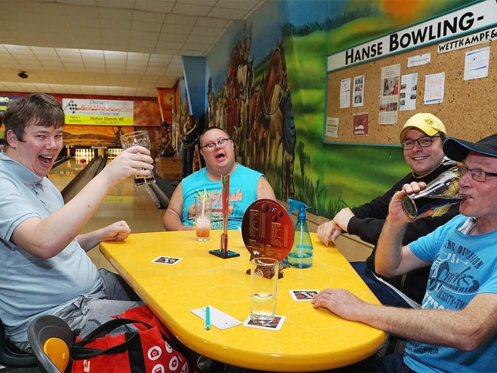 Vier Personen sitzen am Tisch an Bowlingbahn und lachen
