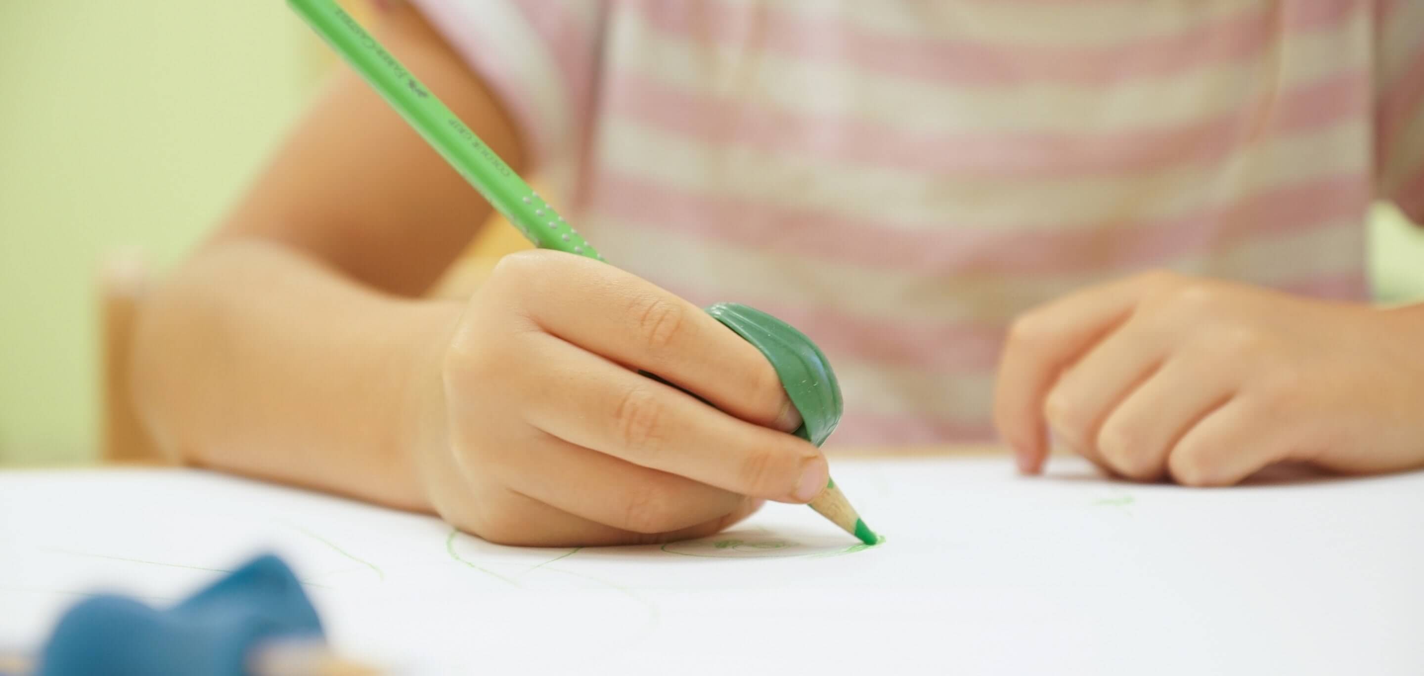 Ein Kind schreibt mit einem grünen Bleistift auf einem Blatt Papier