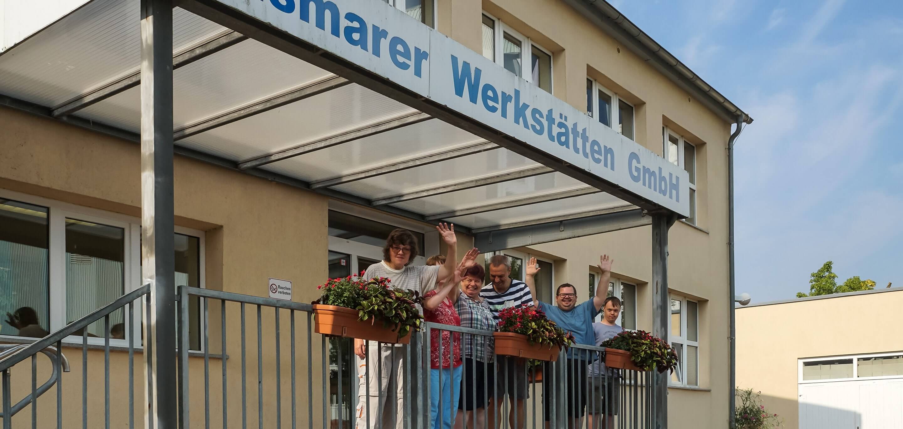 Winkende Menschen stehen am Eingang der Wismarer Werkstätten GmbH